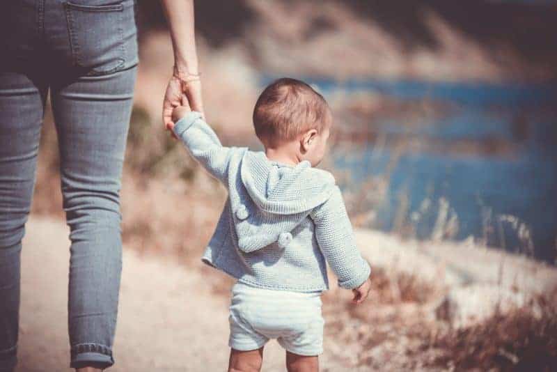 Adult and child walking by water, holding hands.