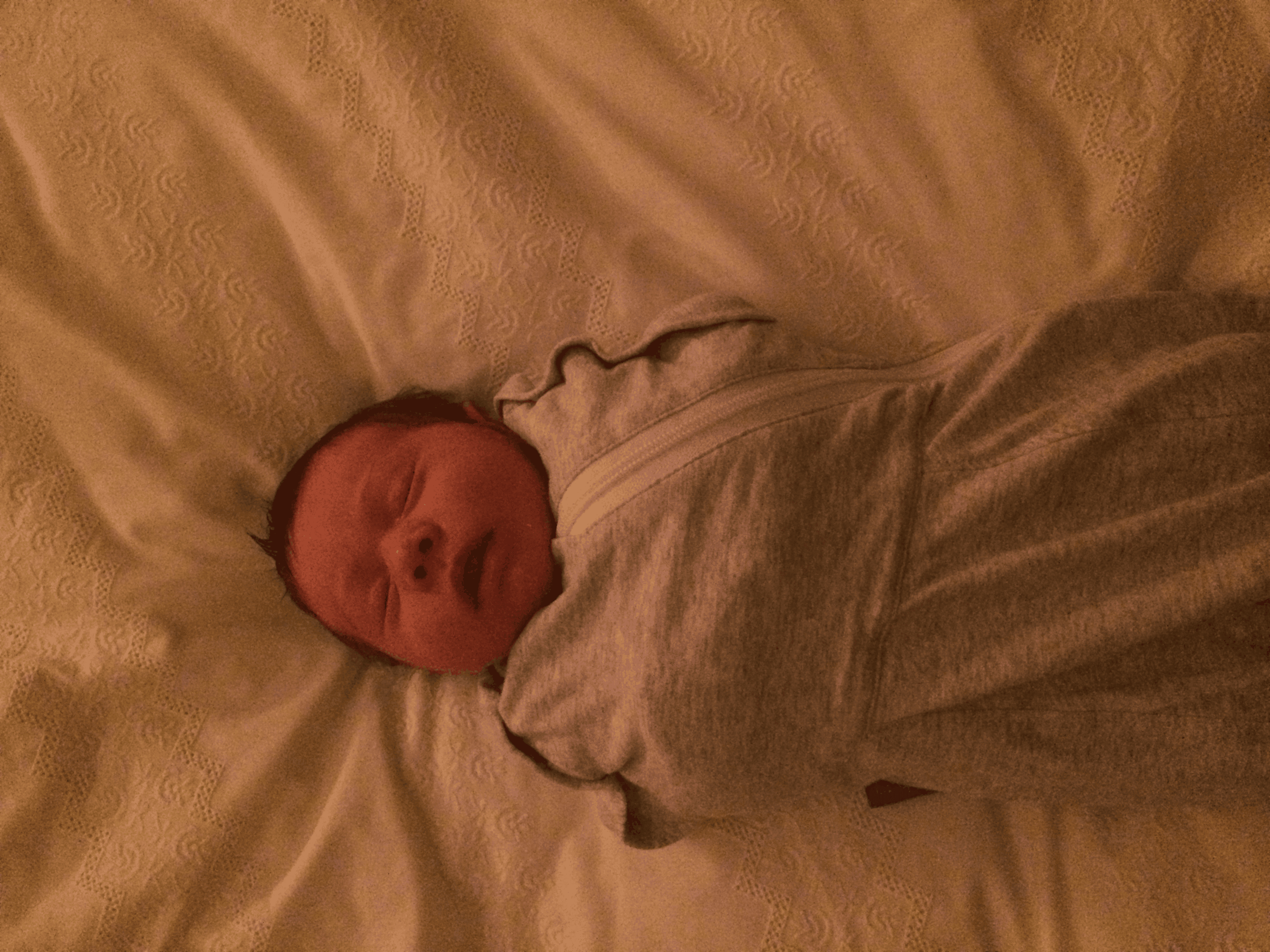 Newborn baby sleeping in swaddle on bed.