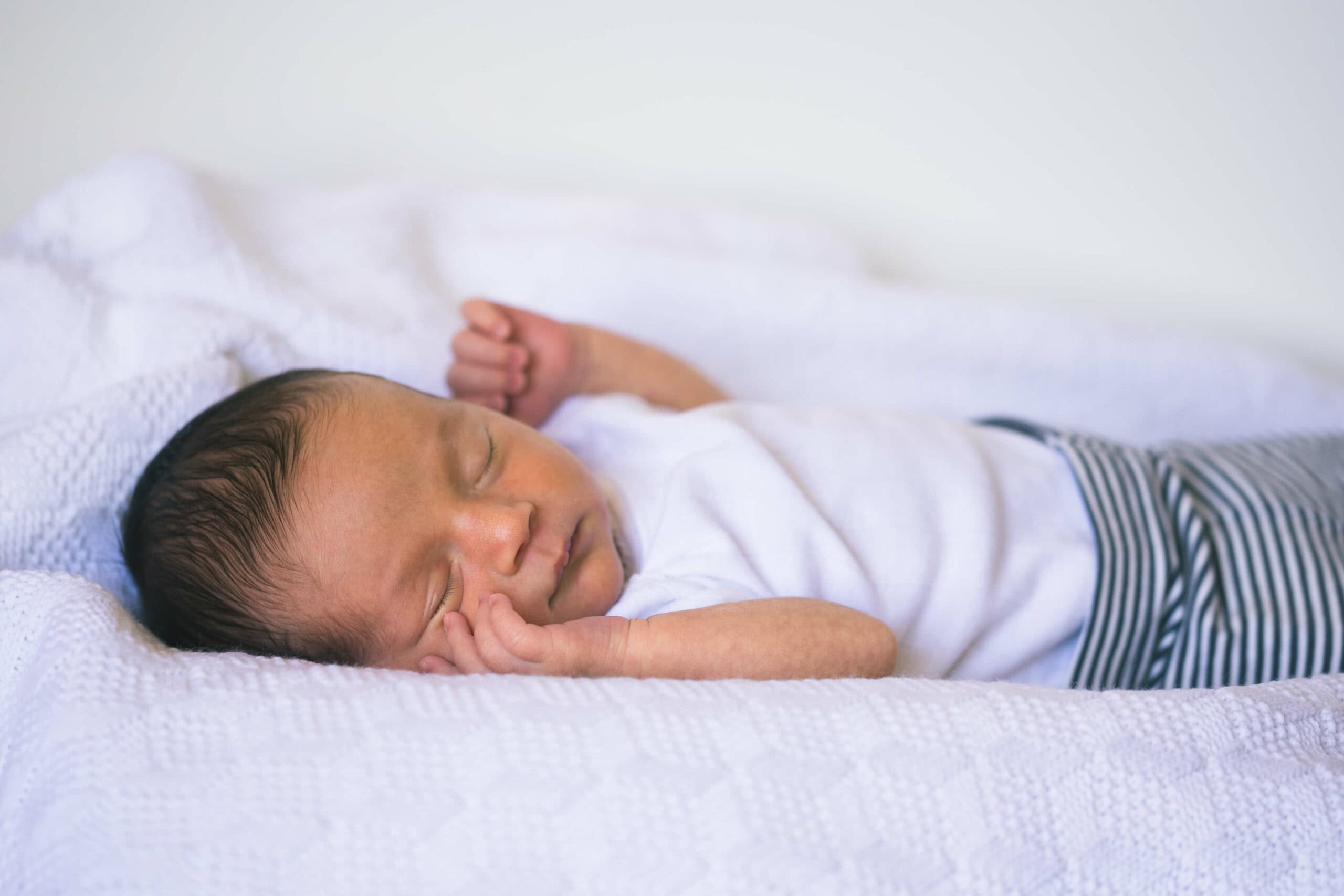 Newborn baby sleeping peacefully on a white blanket.